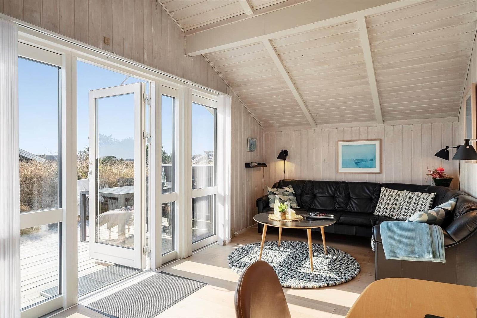 Wohnzimmer mit schwarzer Couch, runder Tisch und Blick auf Balkon.