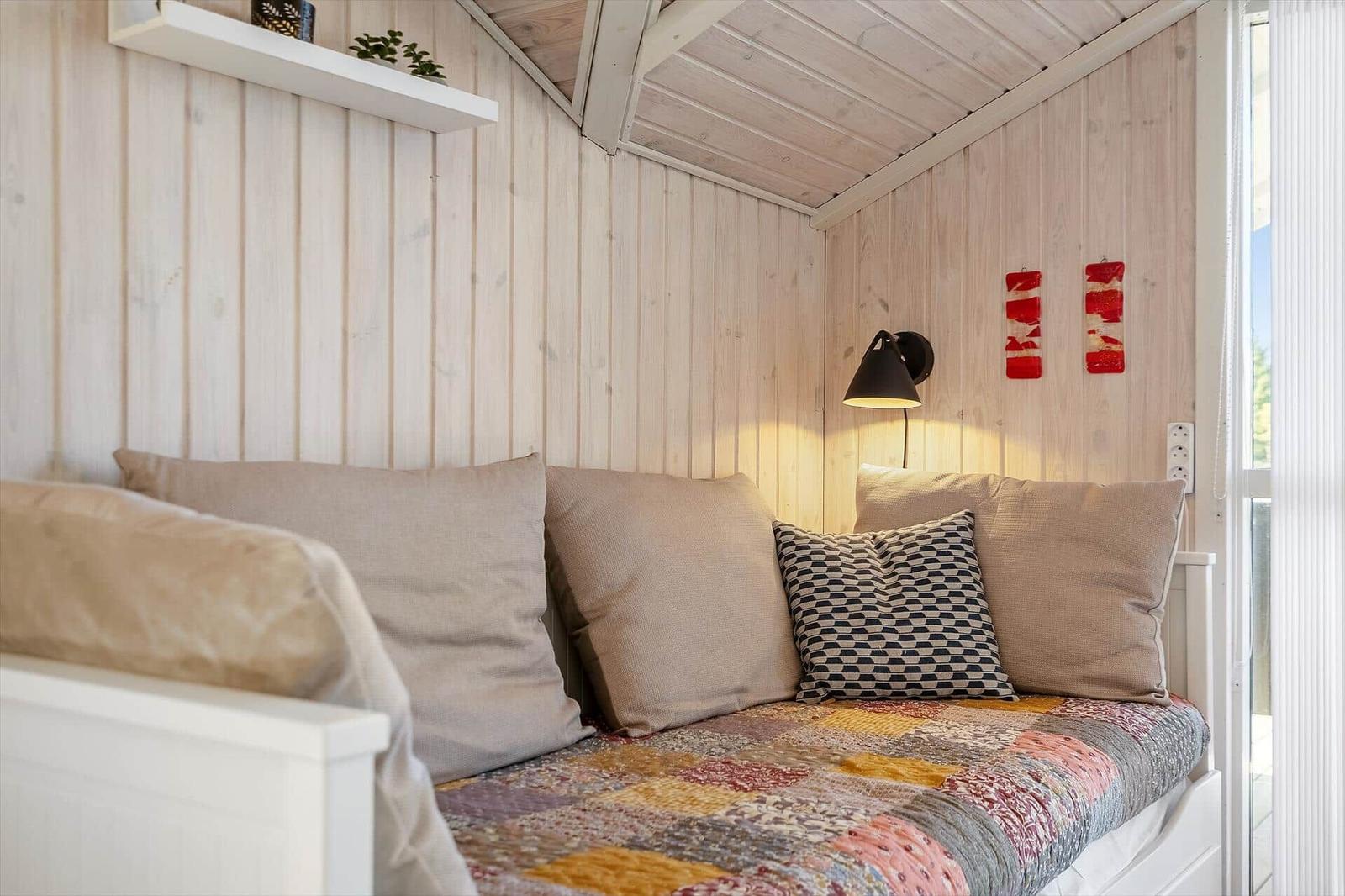 Ein Sofa mit Kissen und Decke in einem holzverkleideten Raum mit Wandlampe und Fenster.