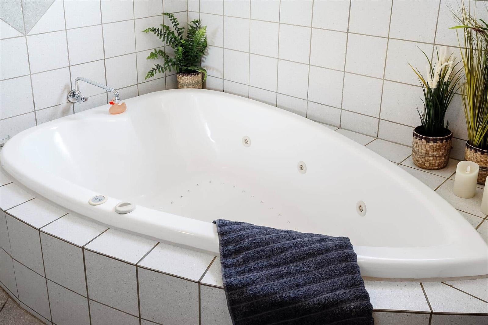 Eine Eckbadewanne mit Duschkopf, Handtuch und Pflanzen.