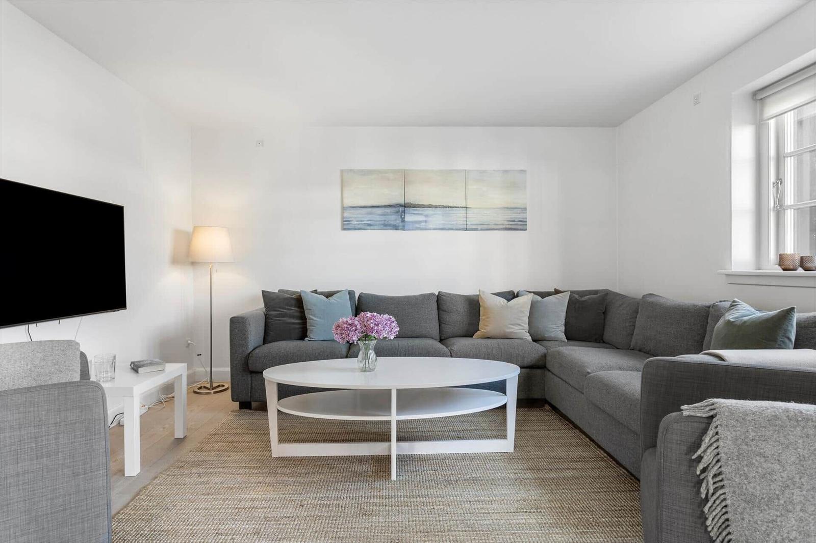 Wohnzimmer mit grauem Sofa, weißem Couchtisch und Wandbild.
