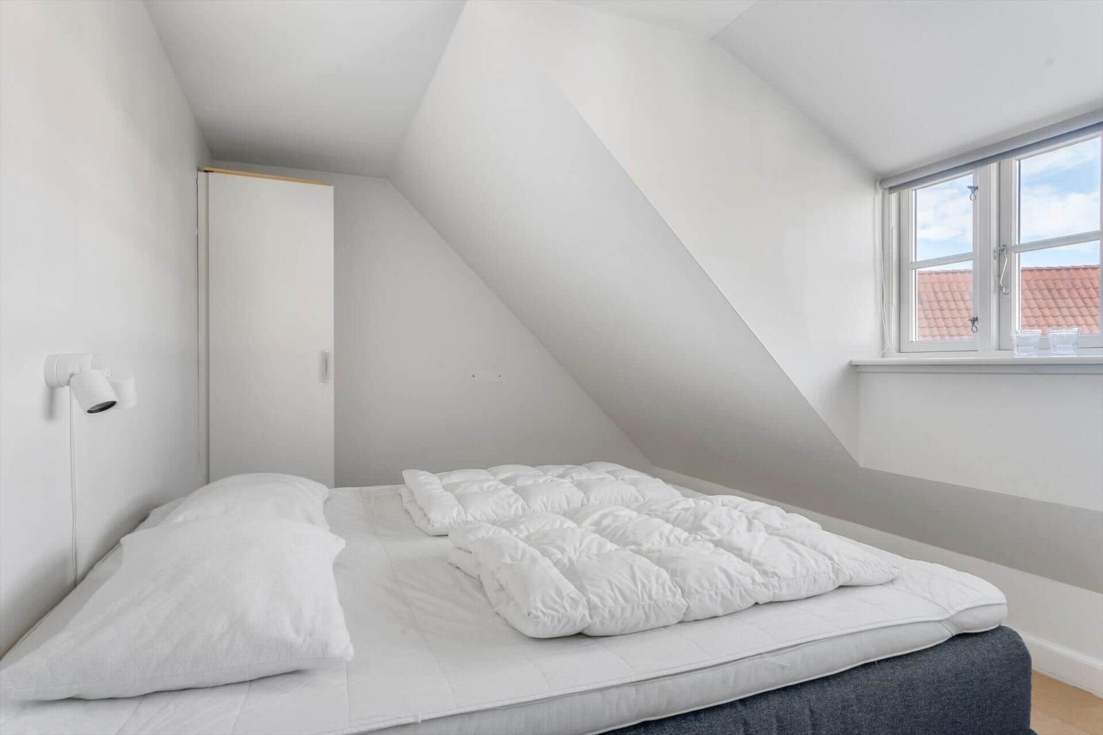 Schlafzimmer mit Dachschrägen, weißem Bett und Fenster mit Blick auf Dach