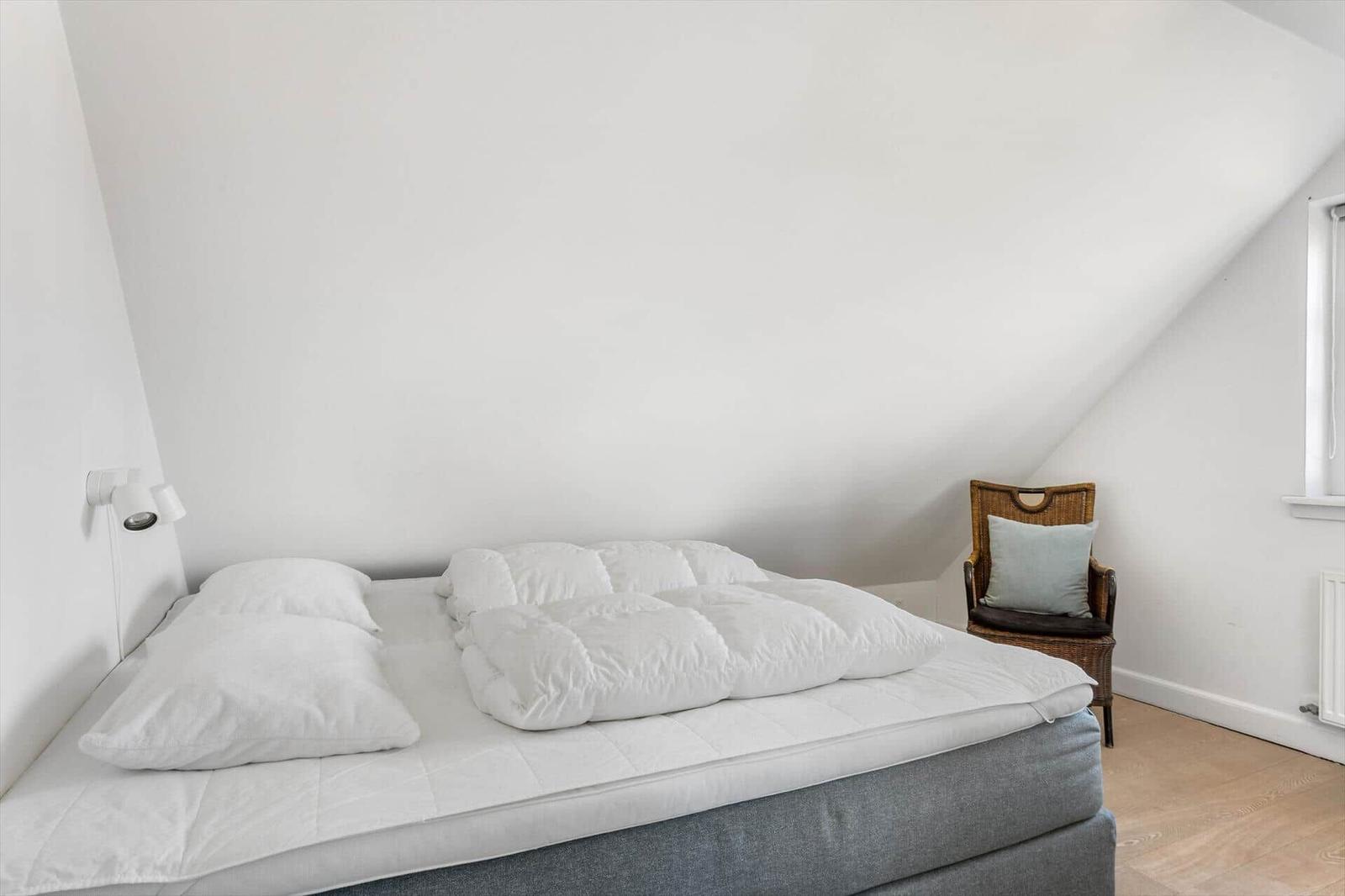 Schlafzimmer mit Dachschrägen, Bett und Stuhl.