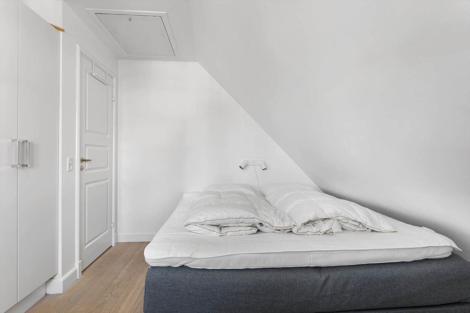 Schlafzimmer mit Dachschräge, Bett, Kleiderschrank und Tür.