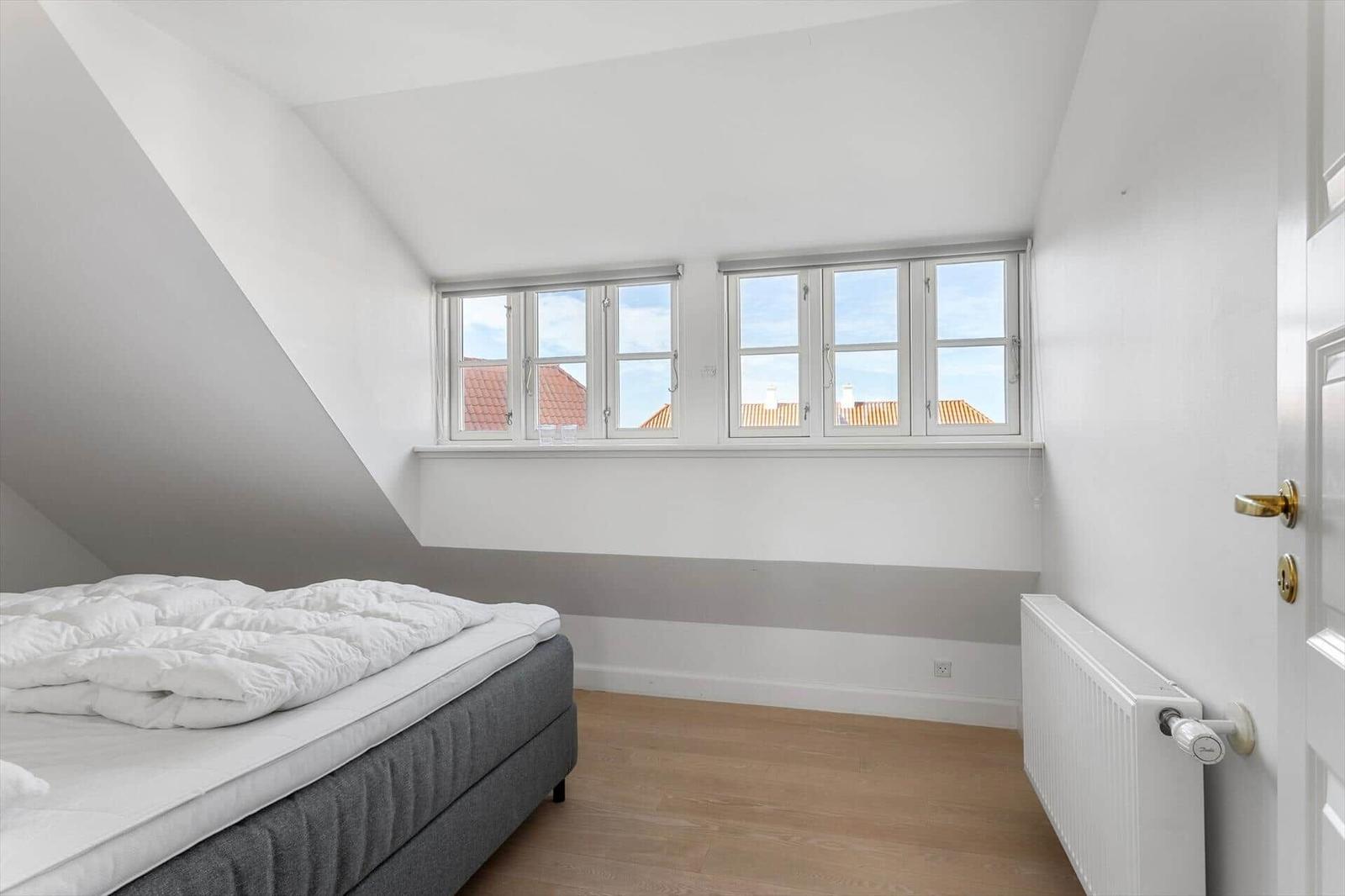 Schlafzimmer mit Dachschrägen, zwei Fenstern und Holzboden.