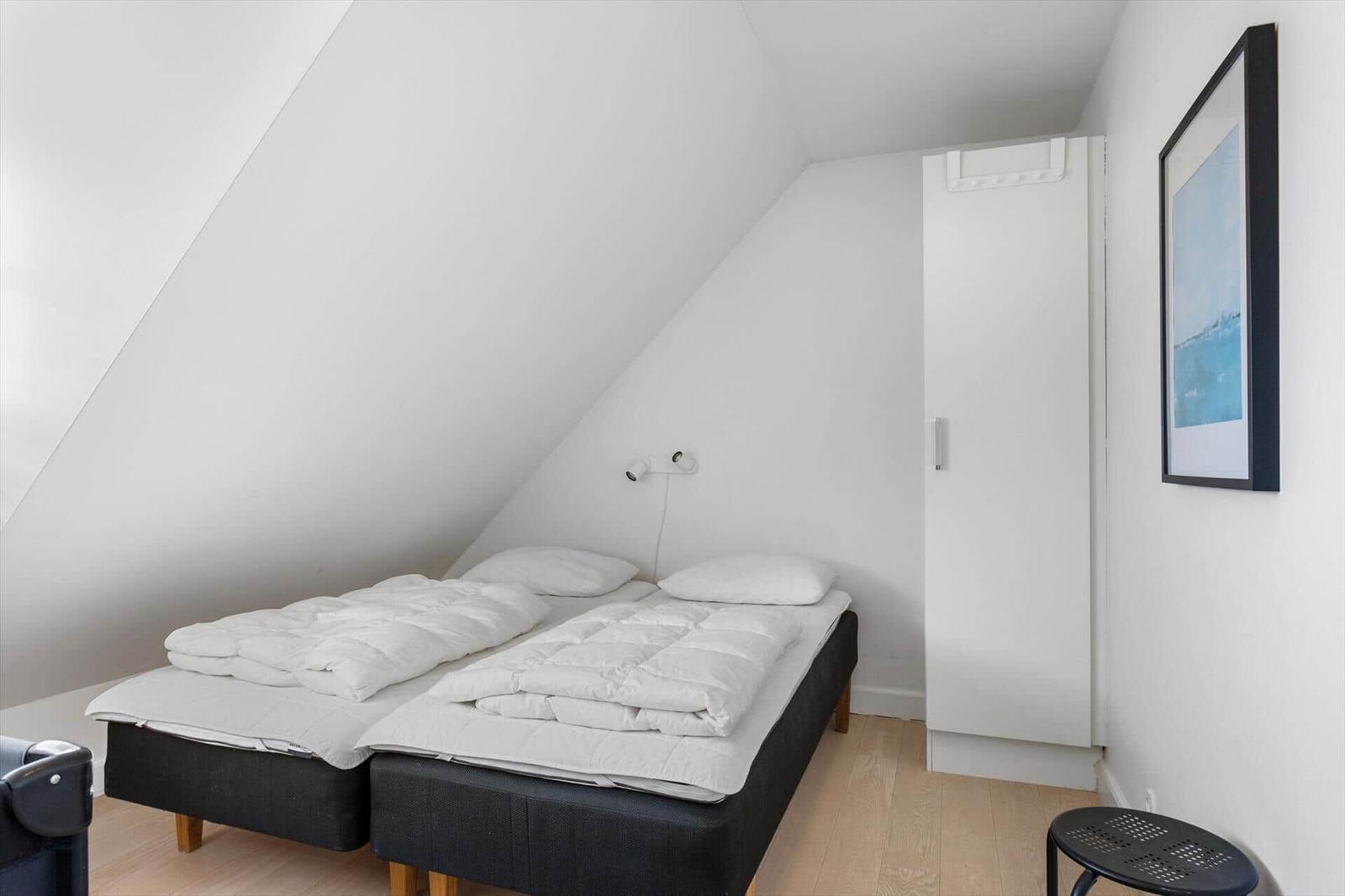 Zimmer mit Doppelbett unter Dachschrägen, weißer Schrank und Wandbild.