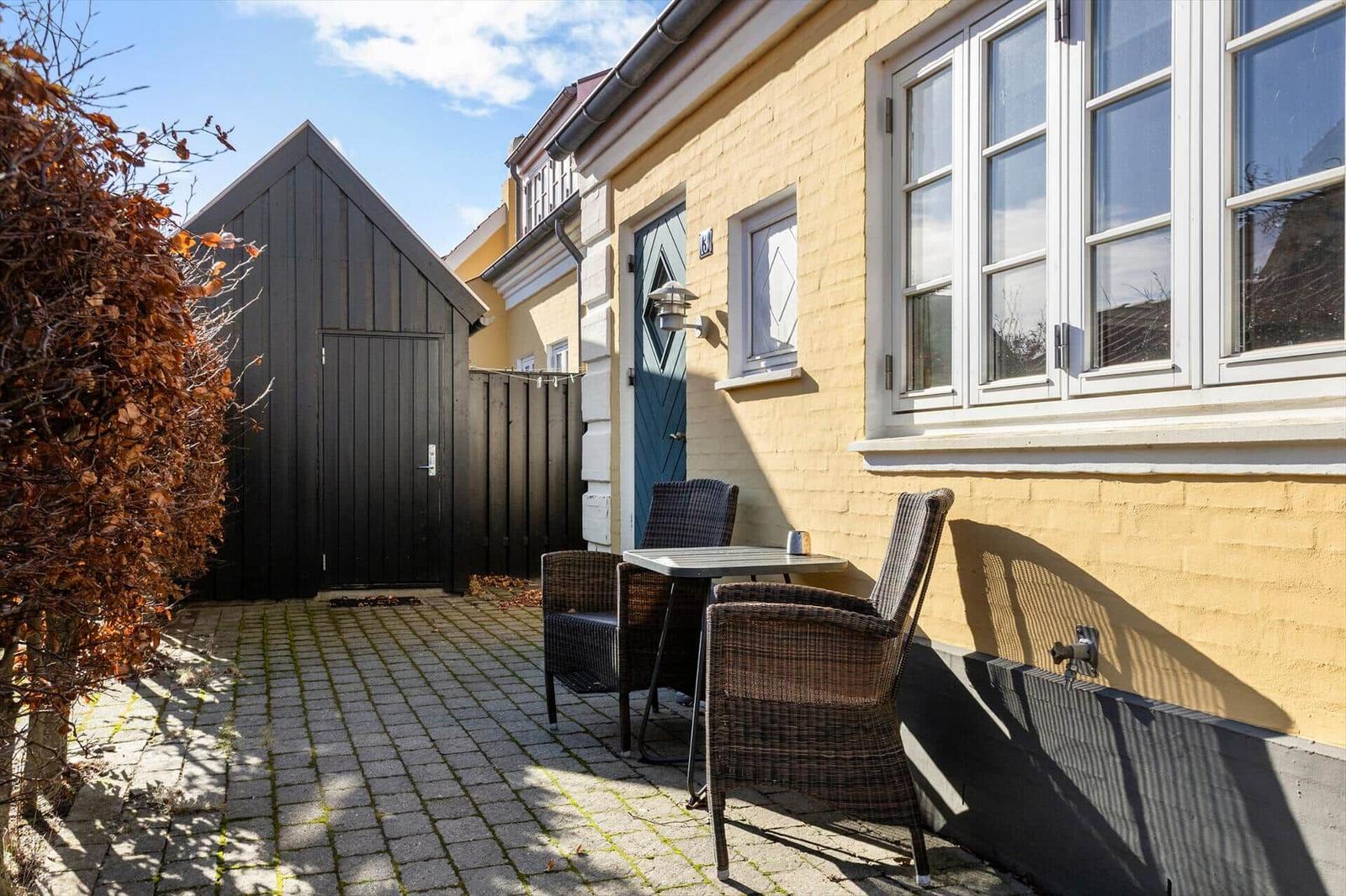 Hinterhof mit Tisch und Stühlen neben gelbem Haus mit blauer Tür.