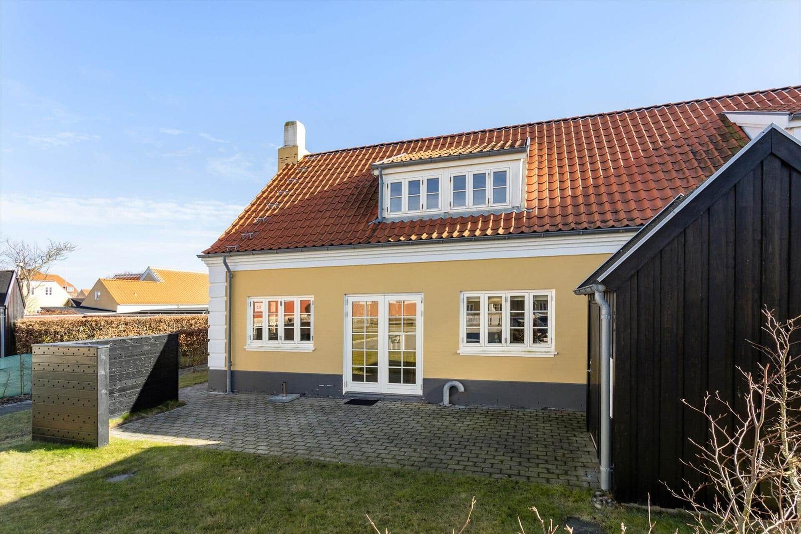 Haus mit gelbem Anstrich, rotem Dach und weißen Fenstern. Vorgarten mit Steinplatten.
