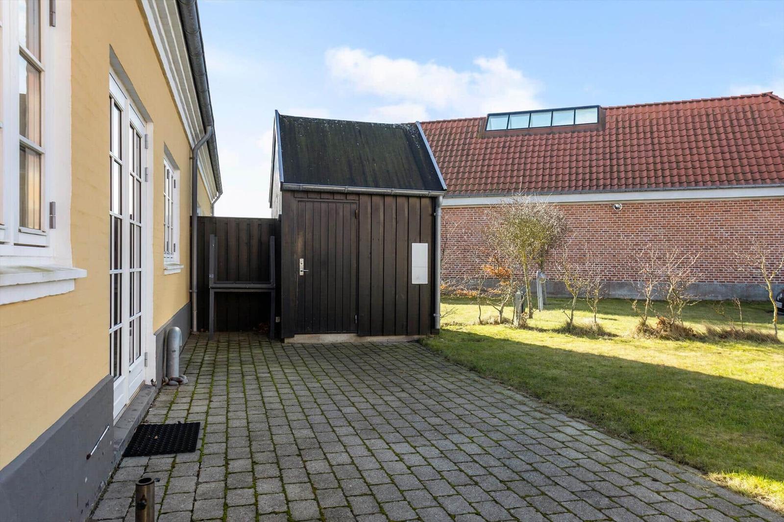 Hinterhof mit Steinweg, Holzschuppen und grünem Rasen vor Backsteinmauer.