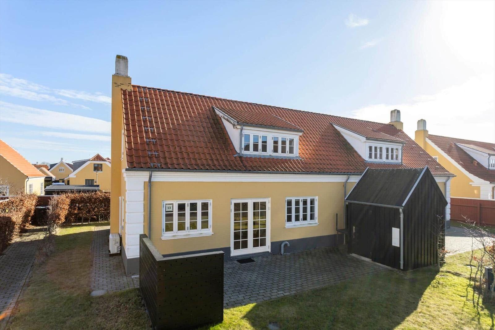 Gelbes Haus mit rotem Dach, weißen Fenstern und kleinem Schuppen.