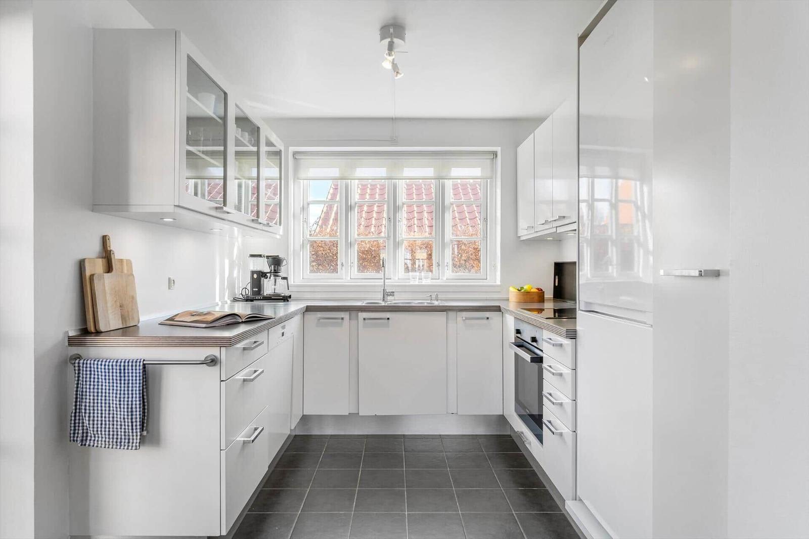 Moderne Küche mit weißen Schränken, dunklem Boden und Fenster mit Blick auf Dächer.