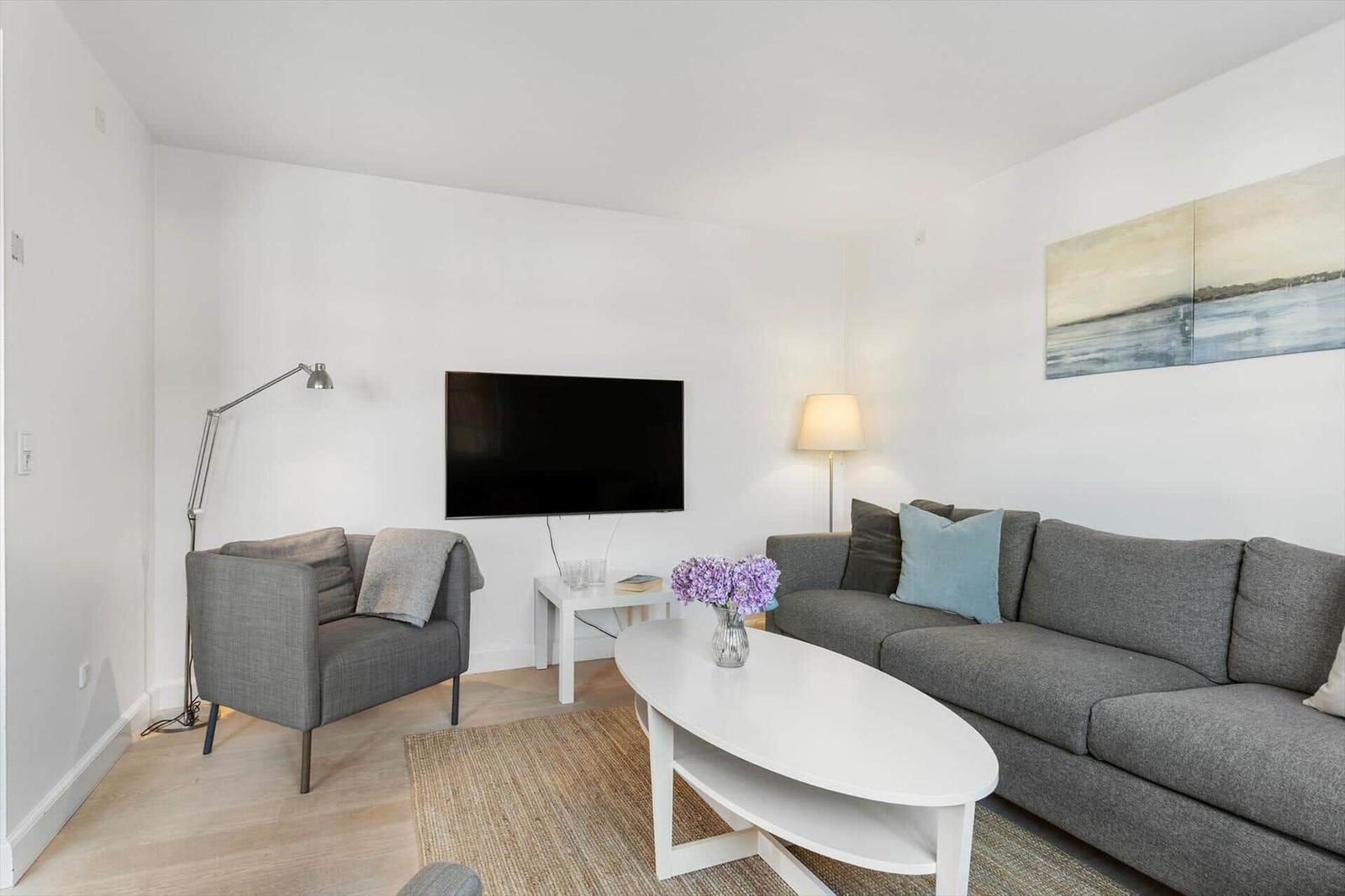 Wohnzimmer mit grauem Sofa, weißem Couchtisch und Fernseher an der Wand.