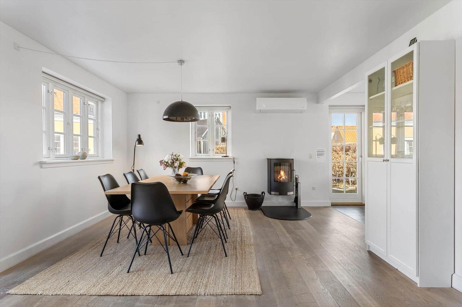 Essbereich mit Tisch, Stühlen und Kaminofen. Holzboden und Fenster sichtbar.