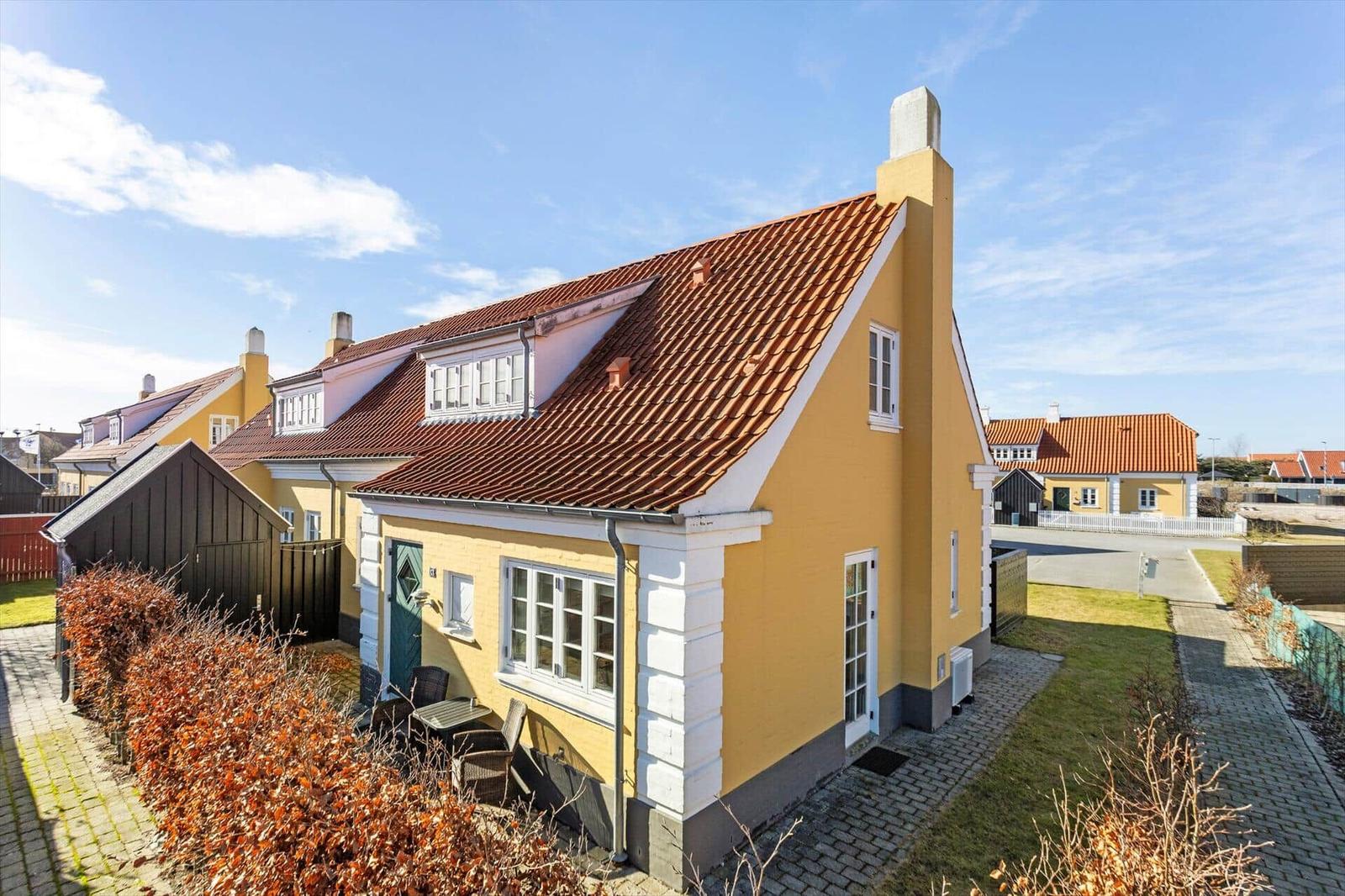 Gelbes Haus mit rotem Dach und kleinem Gartenbereich.
