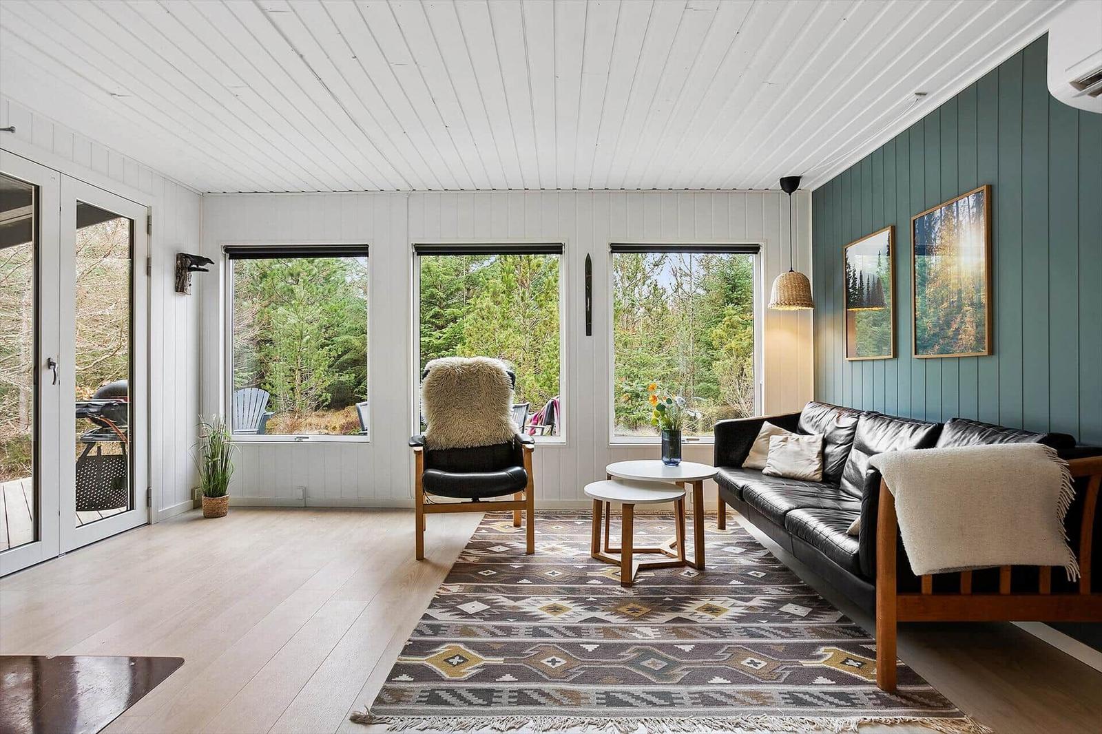 Living room with sofa, armchair, and windows to nature.
