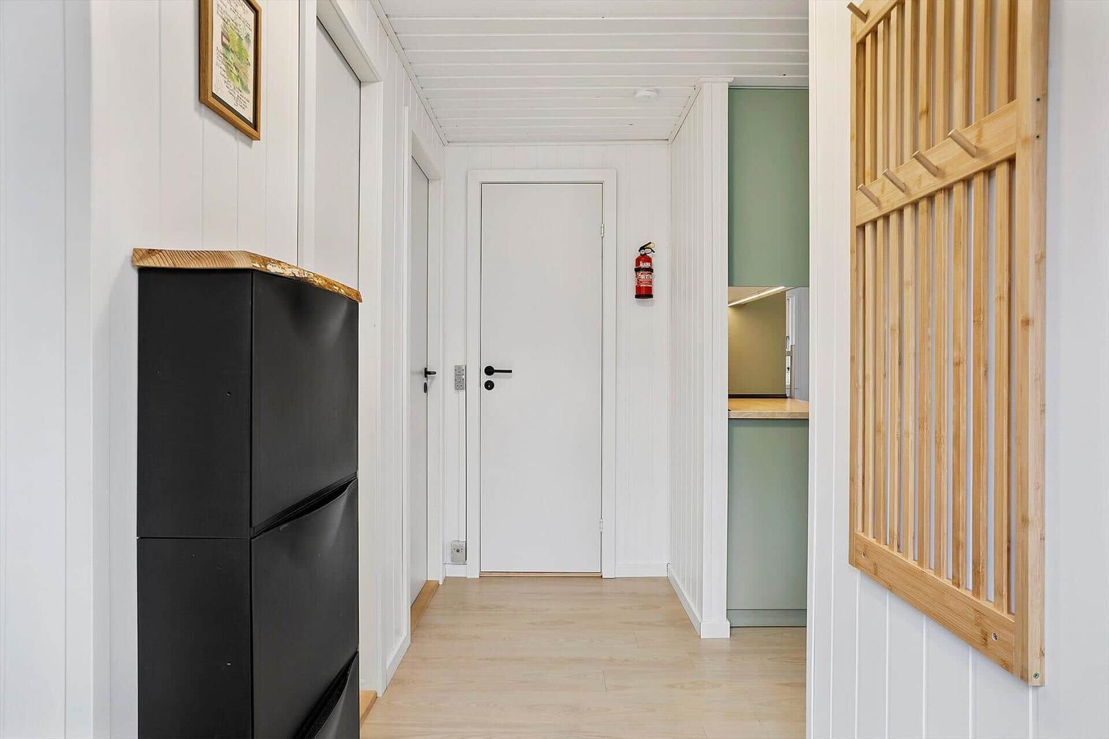 Hallway with black refrigerator, wooden floor, and view into the kitchen.