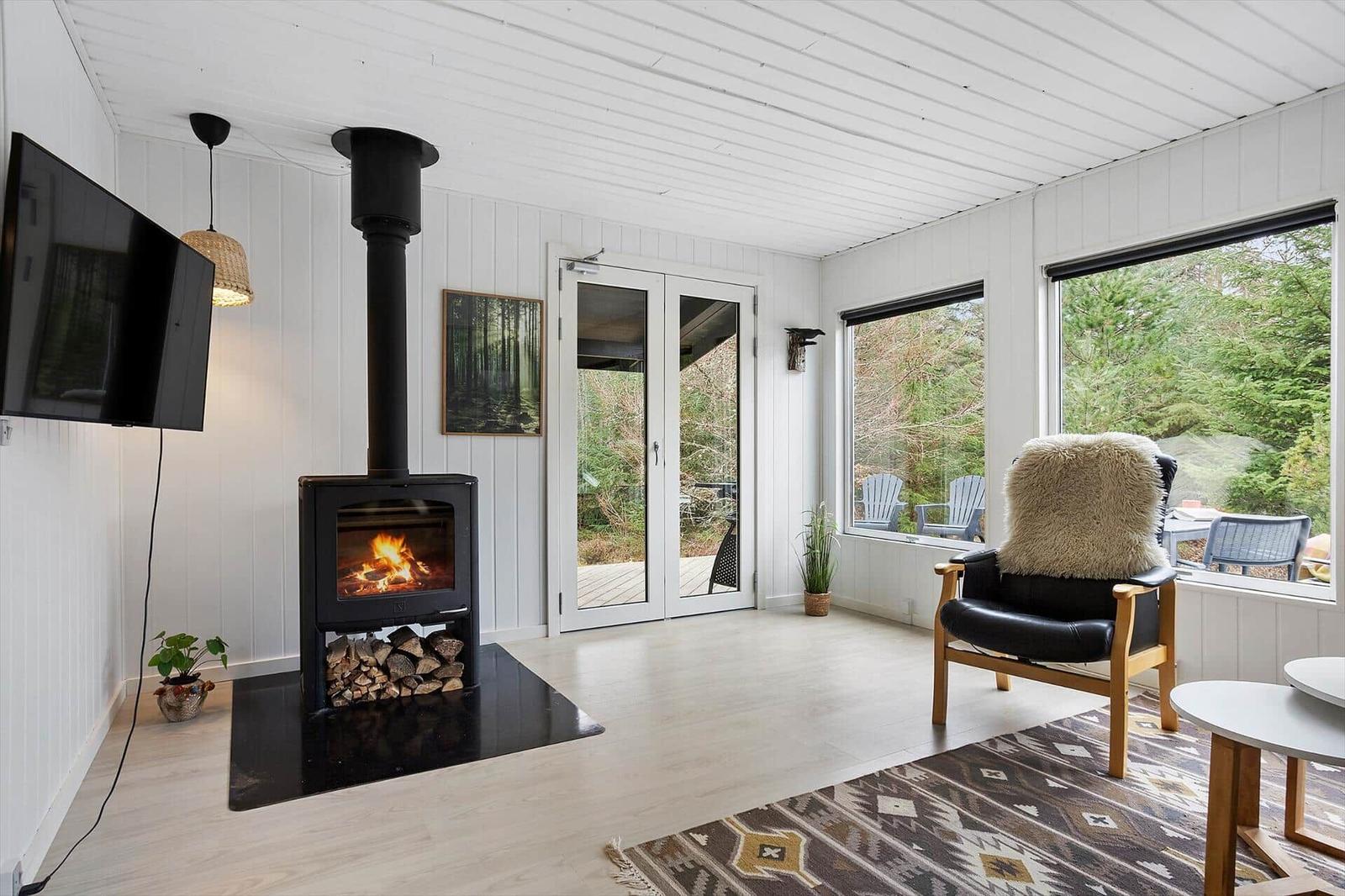 Living room with fireplace, TV, and seating. Large windows offer view of outdoor area.