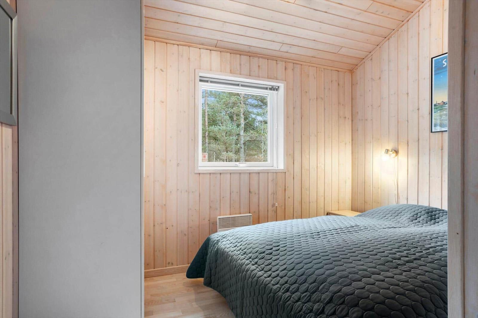Bedroom with wooden walls, bed, and window overlooking the forest.