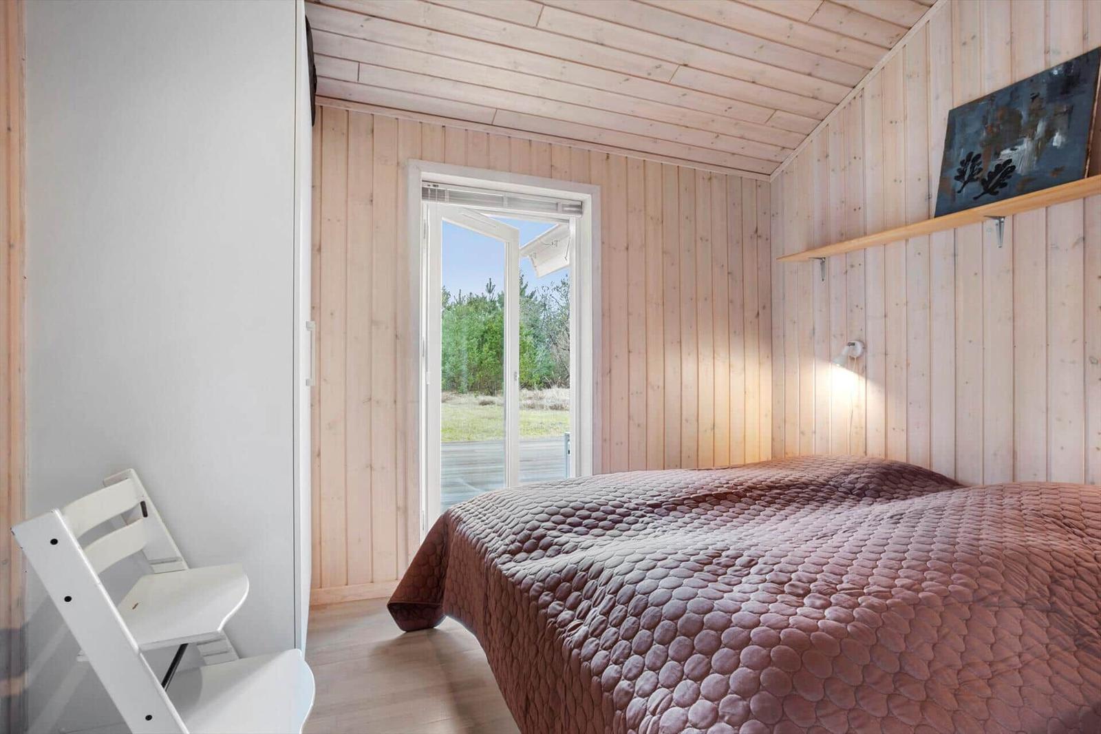 Bedroom with bed, wooden walls, and window to outdoor terrace.