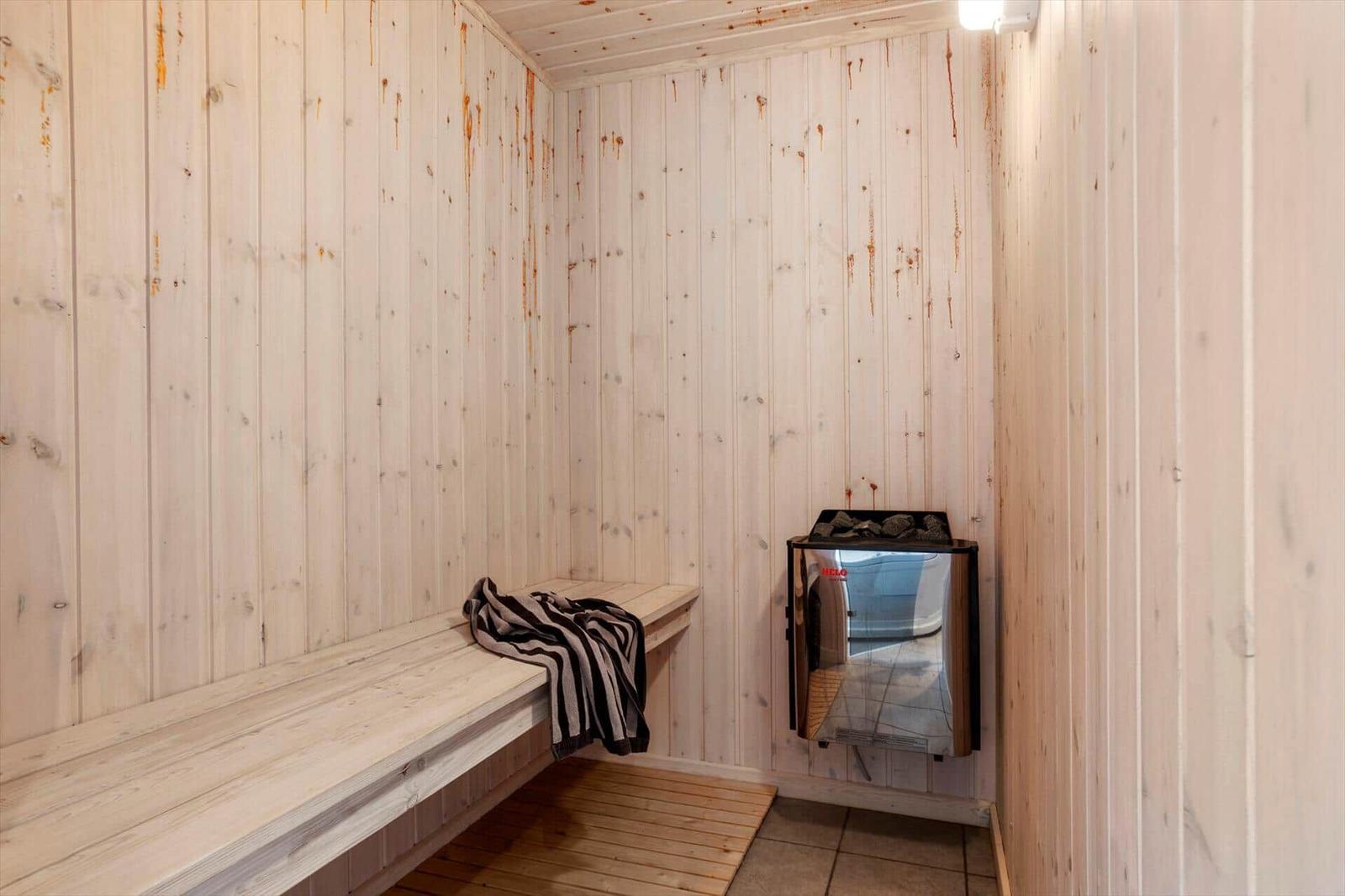 Sauna with wooden walls and bench, beside heater with stones.