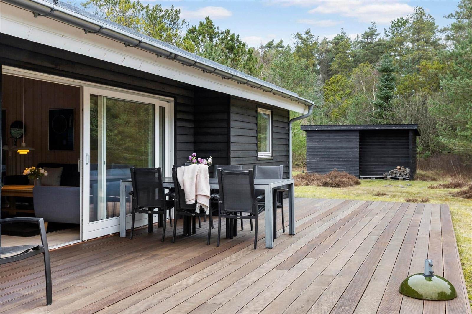 Deck with table and chairs in front of a house with wood siding and sliding doors.