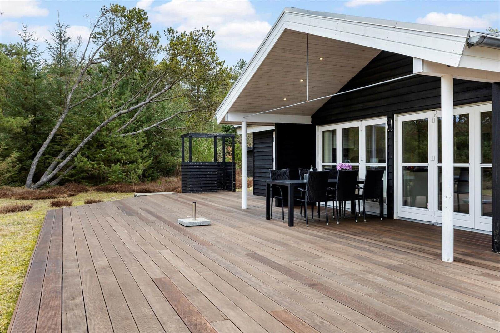 Wooden terrace with table and chairs in front of modern house with large windows.