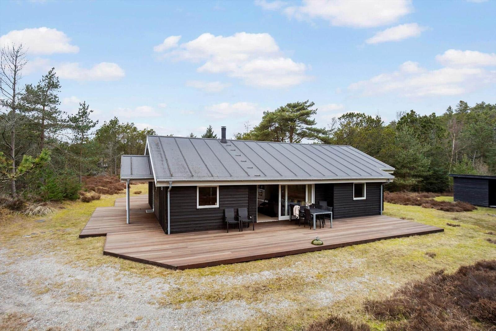 Modern wooden cabin with terrace and garden near forest.