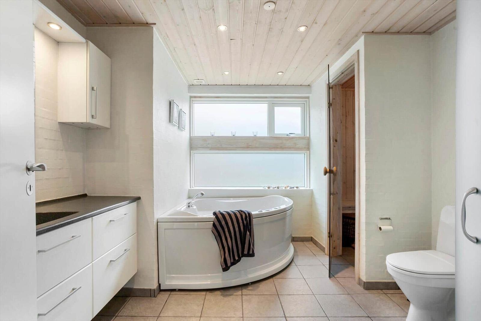 Bathroom with bathtub, toilet, and sauna. Wooden ceiling and window with view.