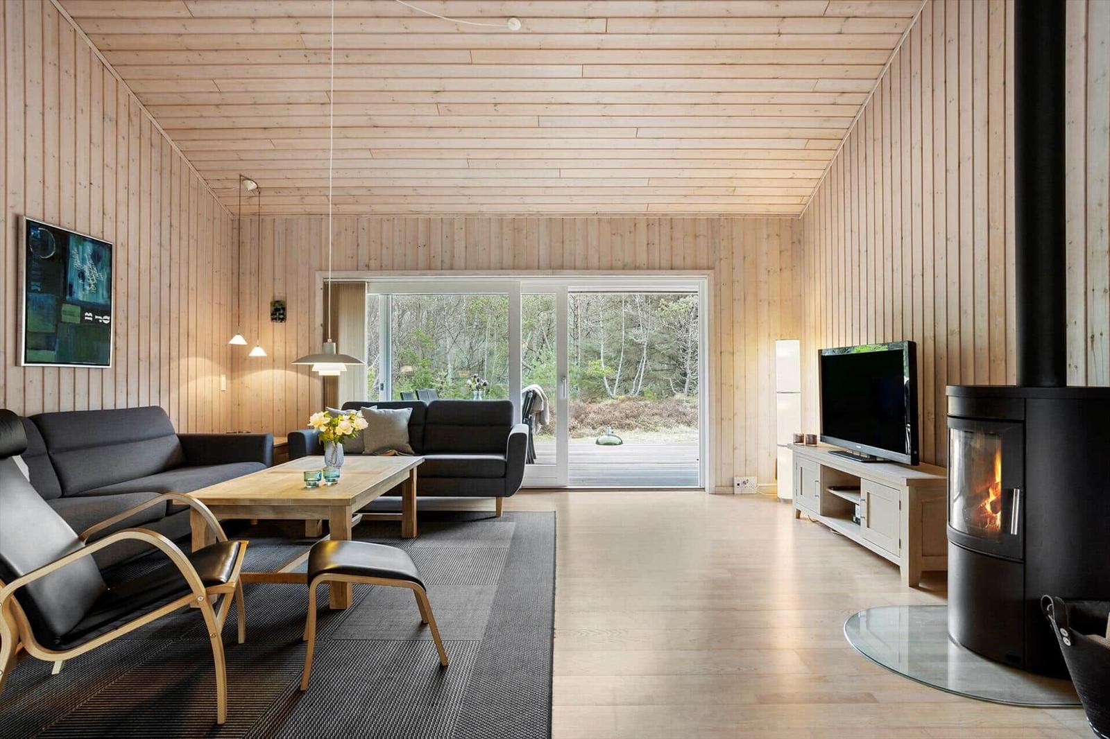 Living room with wood walls, sofa, fireplace, and TV. View of forest through glass door.