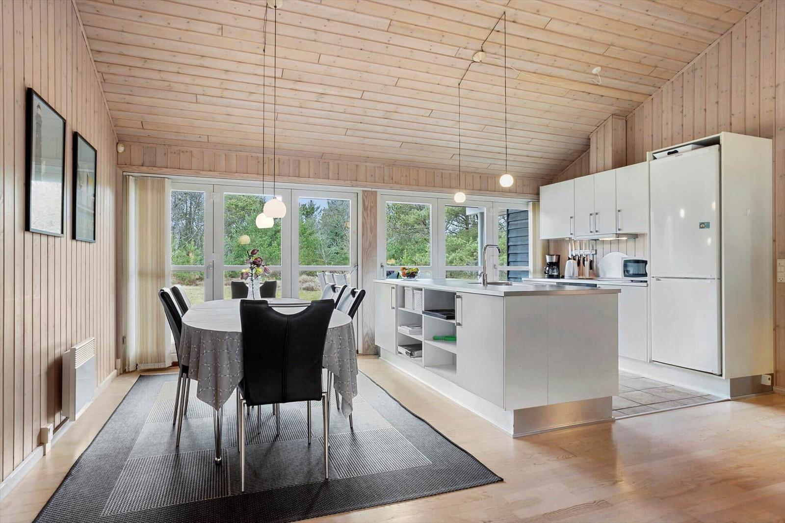 Kitchen and dining area with wooden walls and large windows.