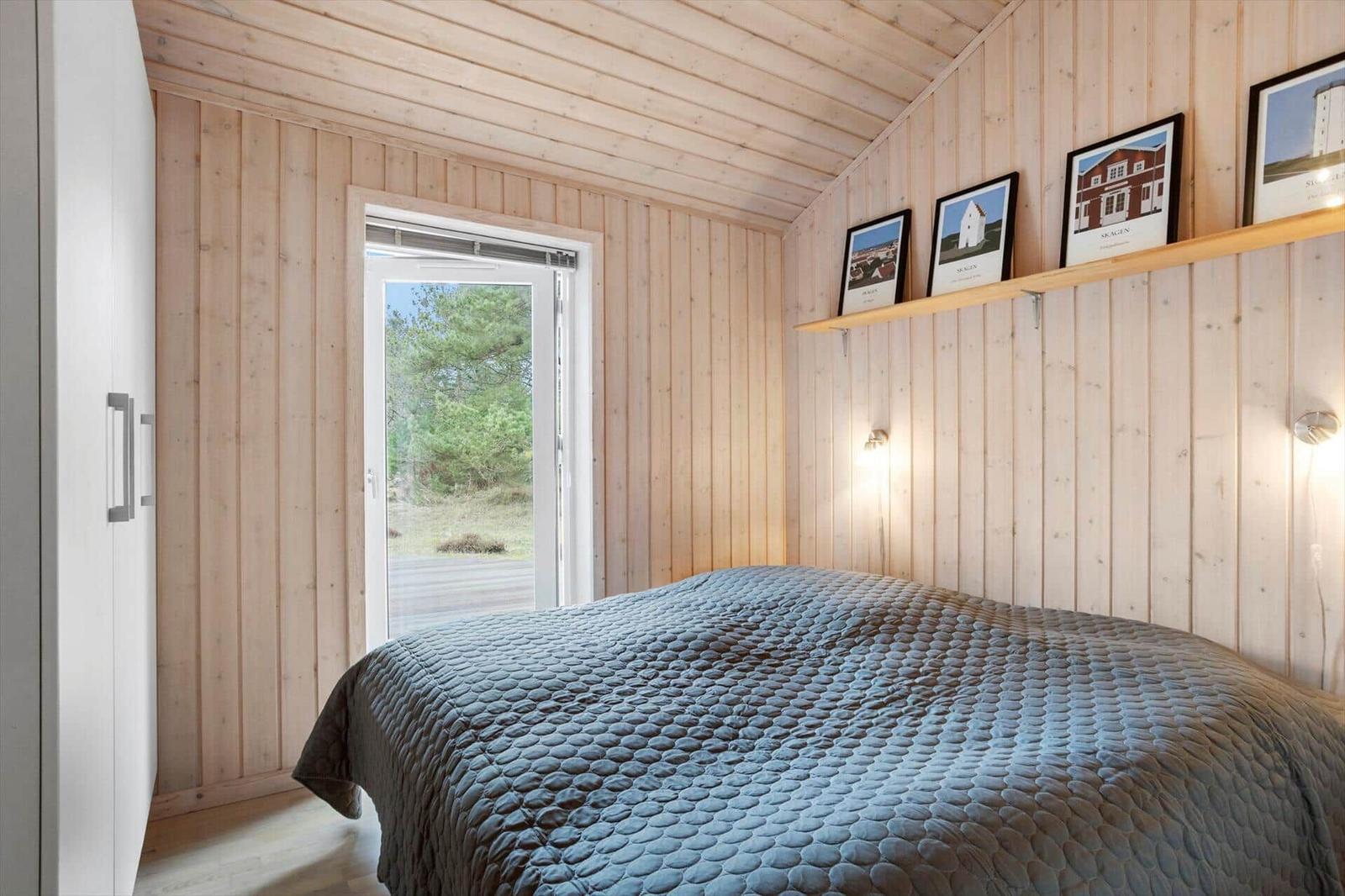 Bedroom with wooden walls, bed, and door to the garden.