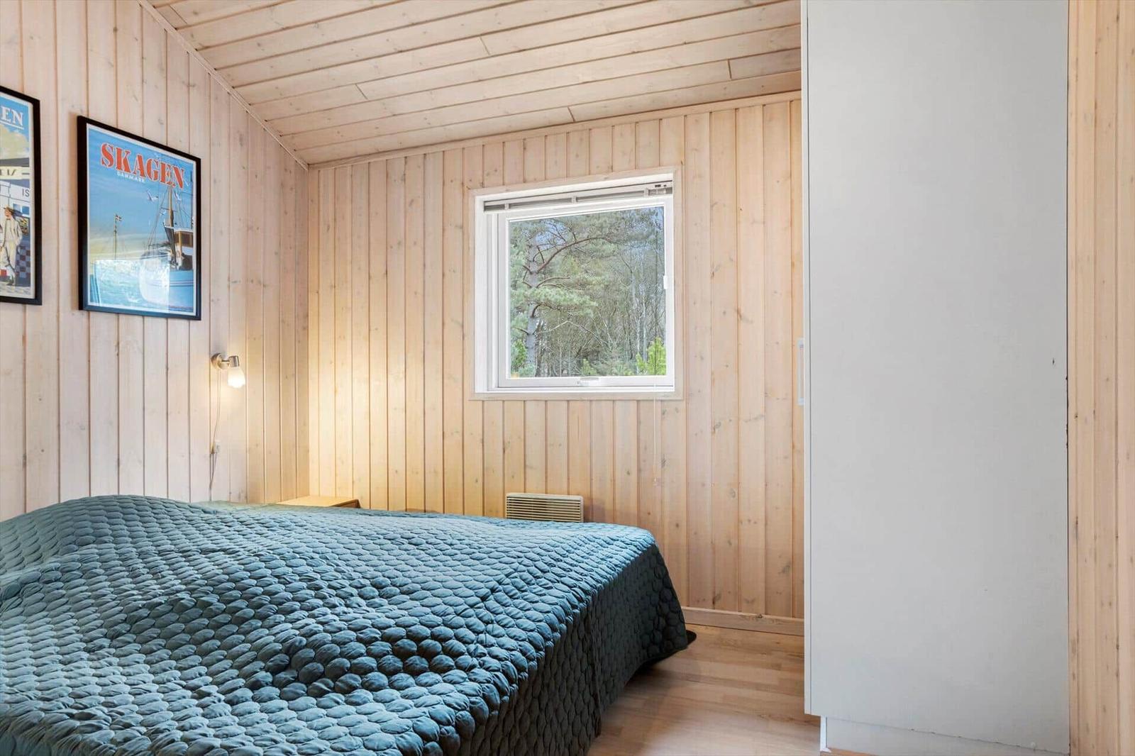 Bedroom with wooden walls, bed, and window to the forest.