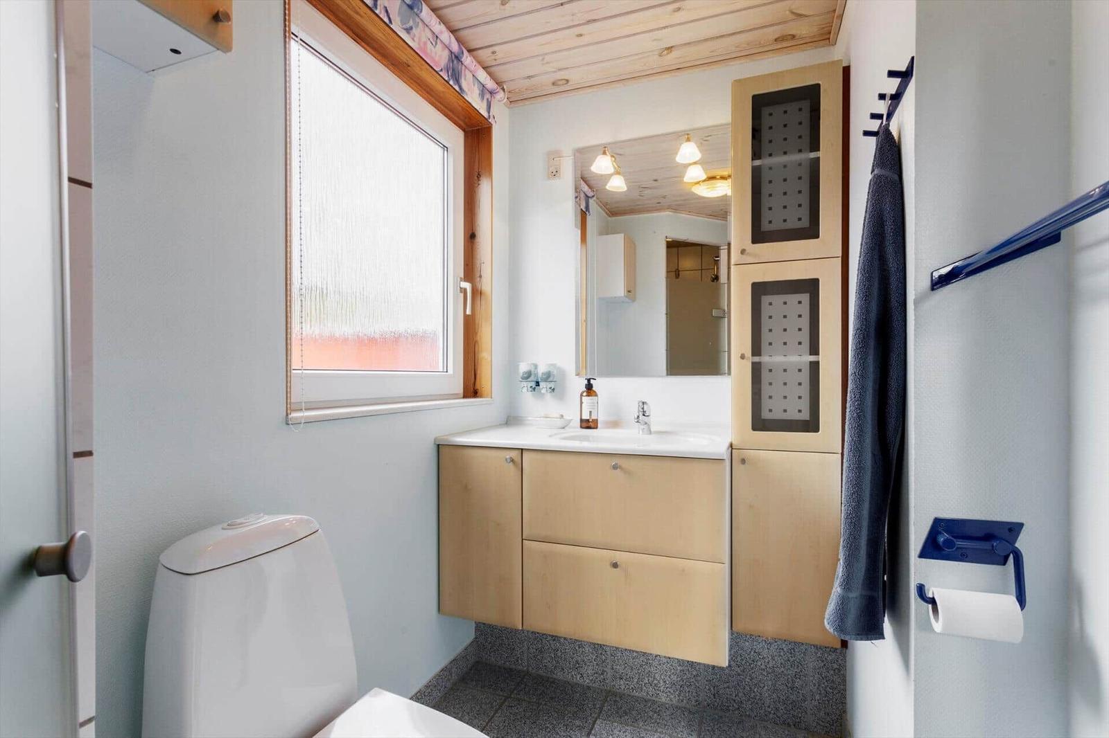 Bathroom with sink, mirror, toilet, and window.