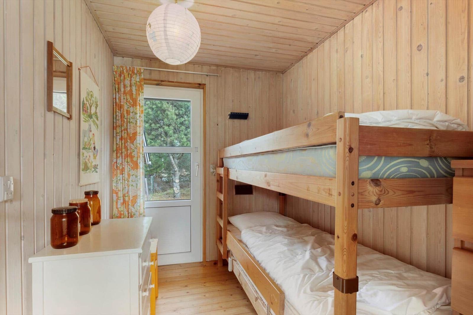 A bedroom with a bunk bed, wooden walls, and a window.