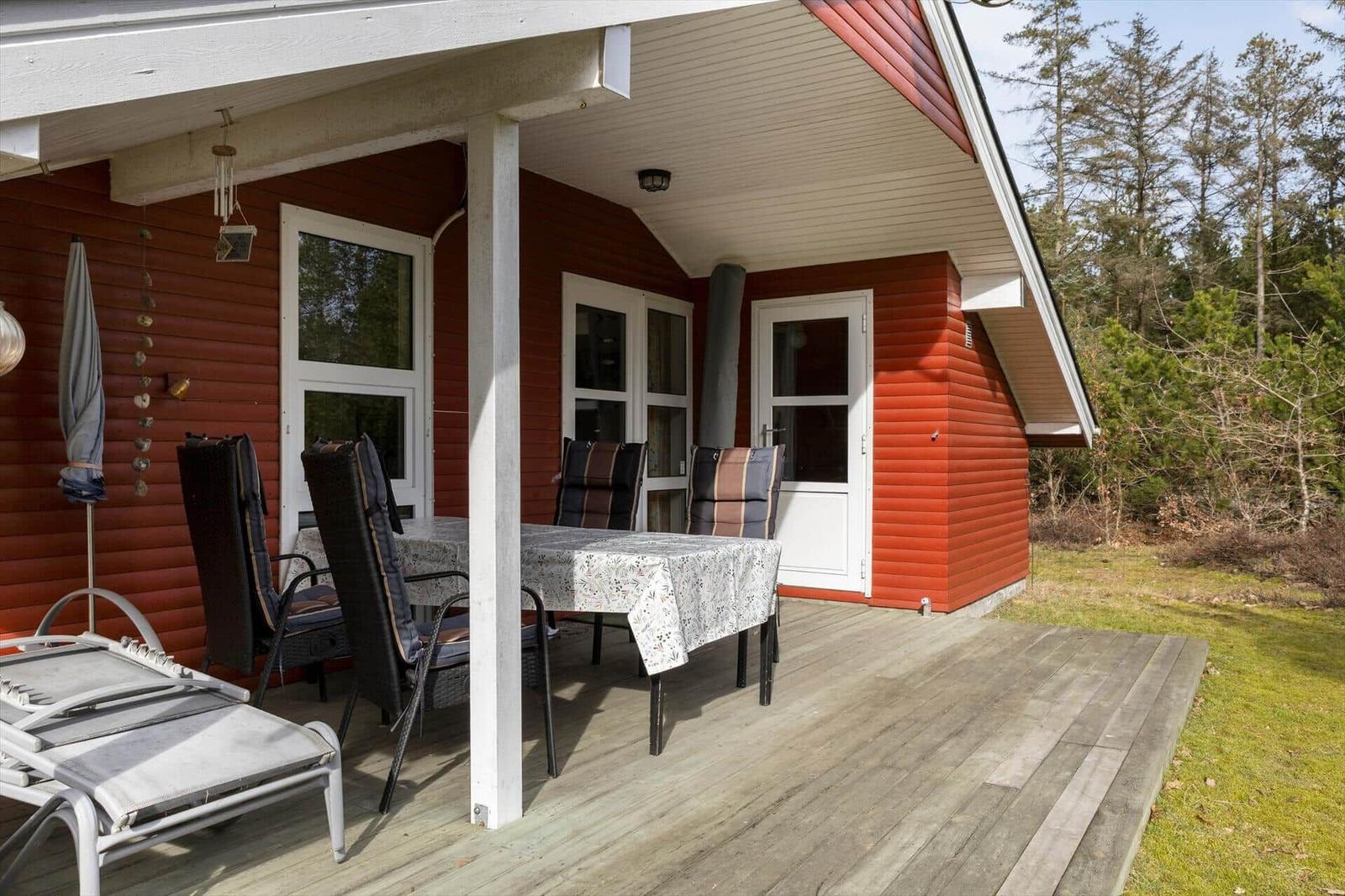 Red wooden house with deck, table, chairs, and lounge chair outside.