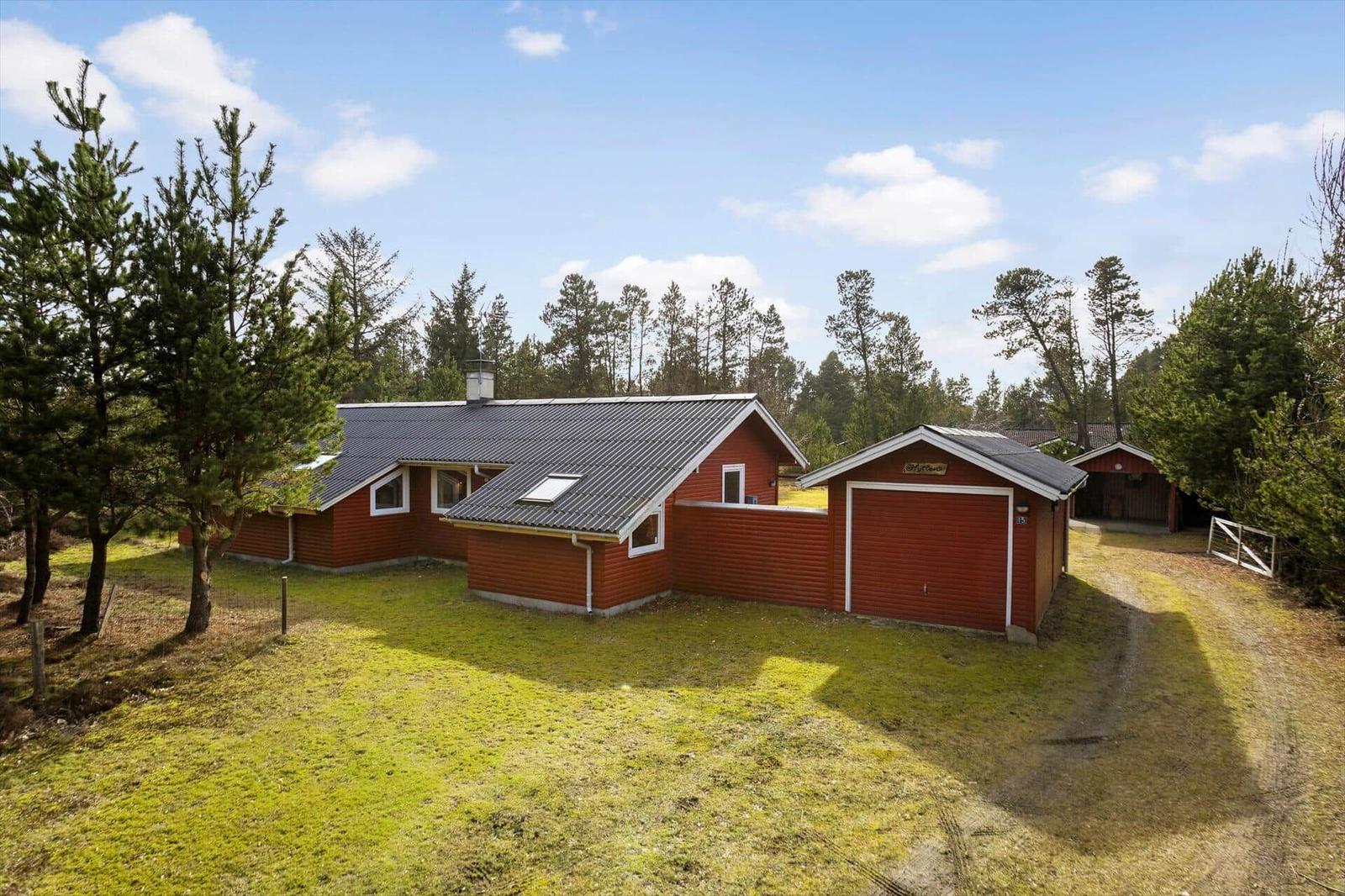 Red wooden house with garage and forest in the background.