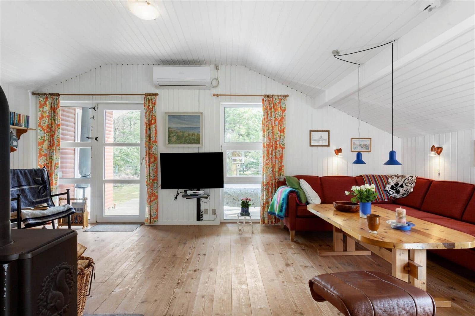 Living room with red sofa, wooden table, and TV. Wooden floor and white walls.