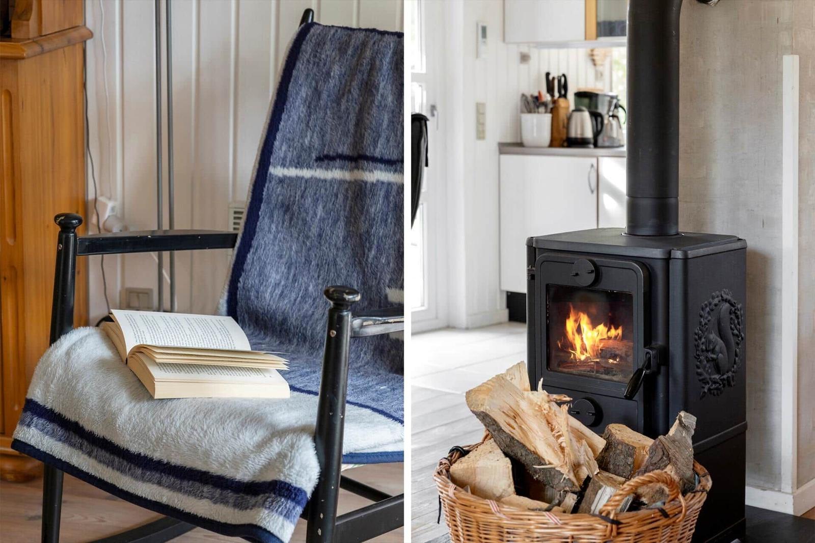 Black stove with firewood and lit fire. Chair with book and blankets.