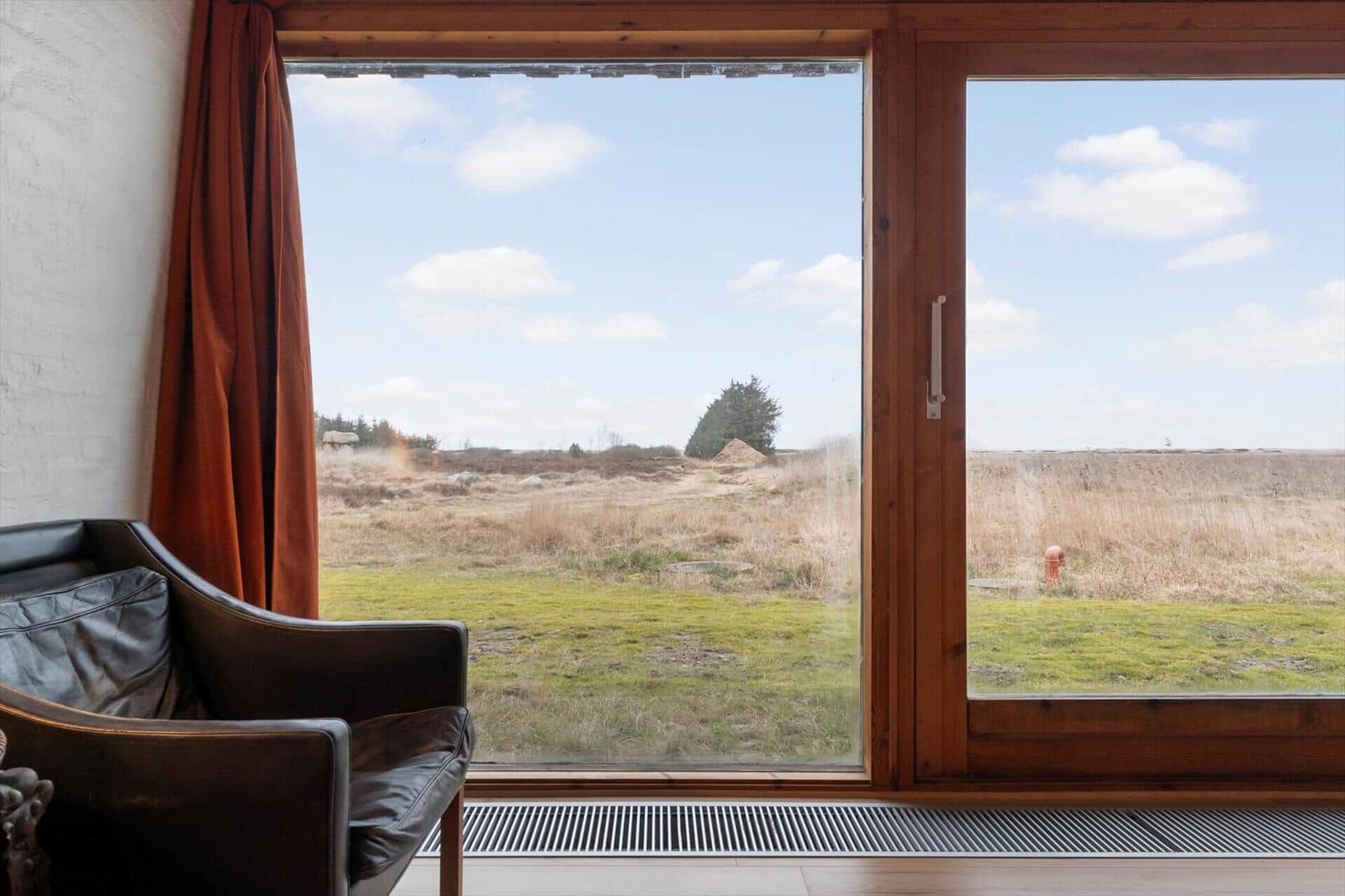 Ein braunes Sofa vor einem großen Fenster mit Blick auf eine Wiese und einen Baum.