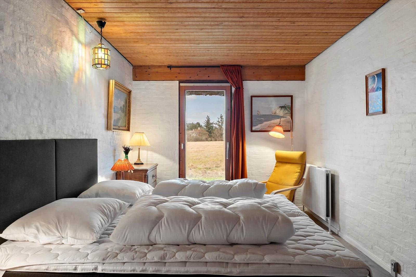 Schlafzimmer mit Bett, Fenster und gelber Sessel.