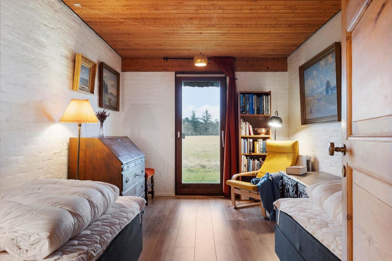 Zimmer mit zwei Betten, Bücherregal und Tür zum Garten.