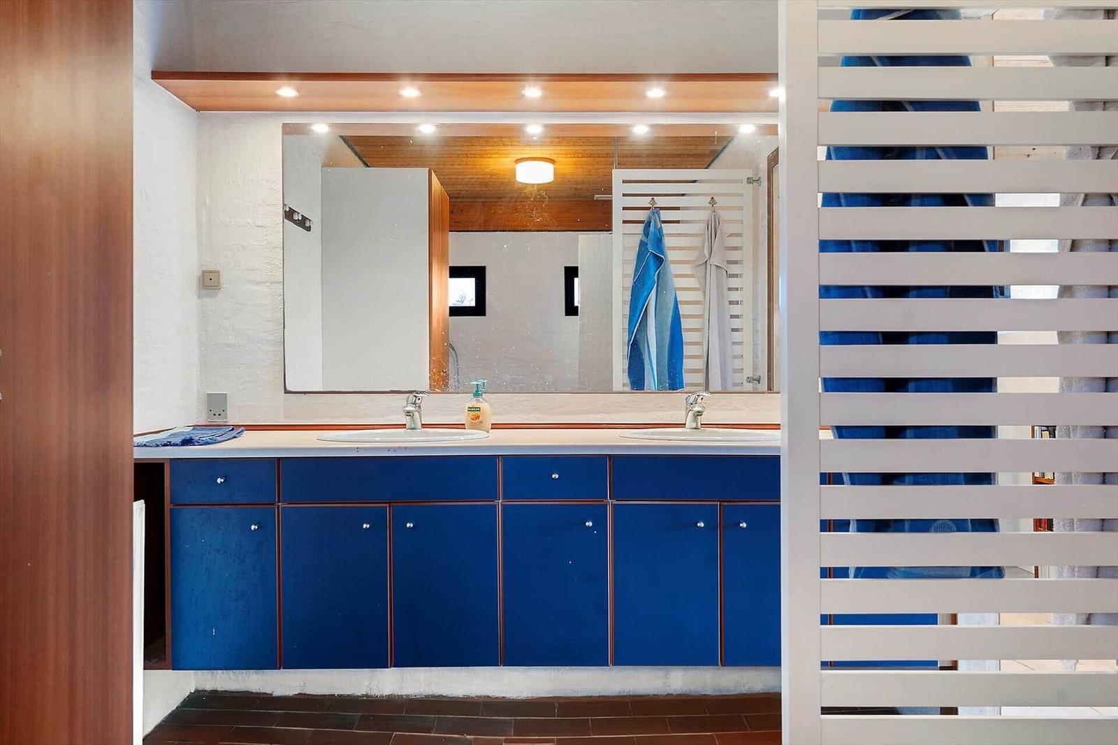 Badezimmer mit blauem Waschbeckenunterschrank und Spiegel. Doppelwaschbecken und Handtuchhalter sichtbar.