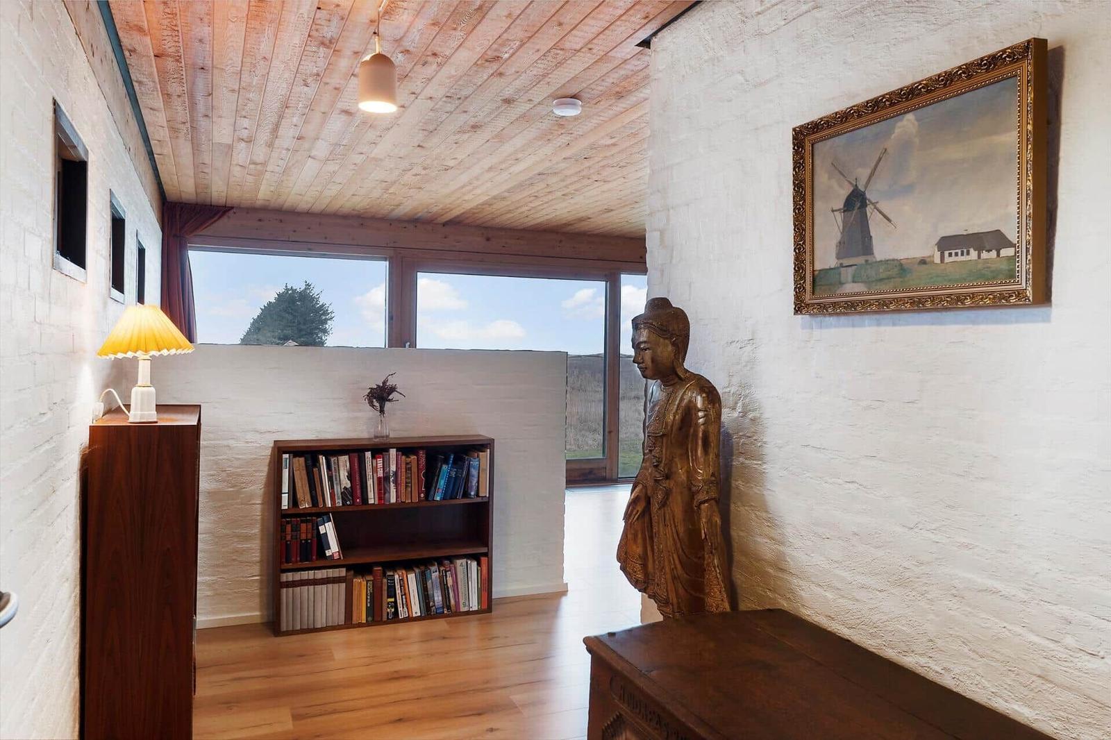 Raum mit Holzboden, Bücherregal, Statue und Wandbild mit Windmühle.