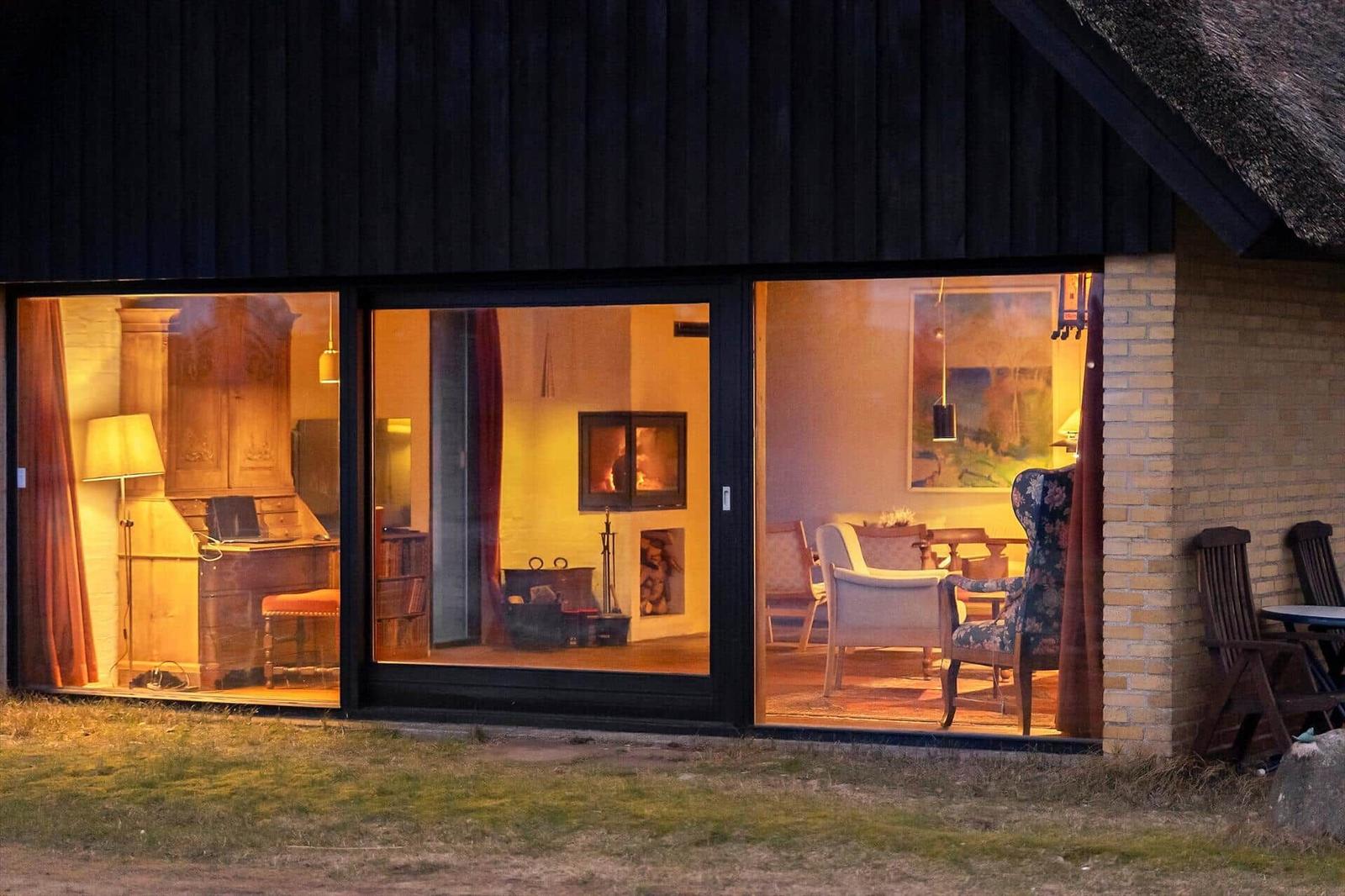 Durch große Fenster ist das Innere mit Kamin, Stühlen und Möbeln sichtbar.