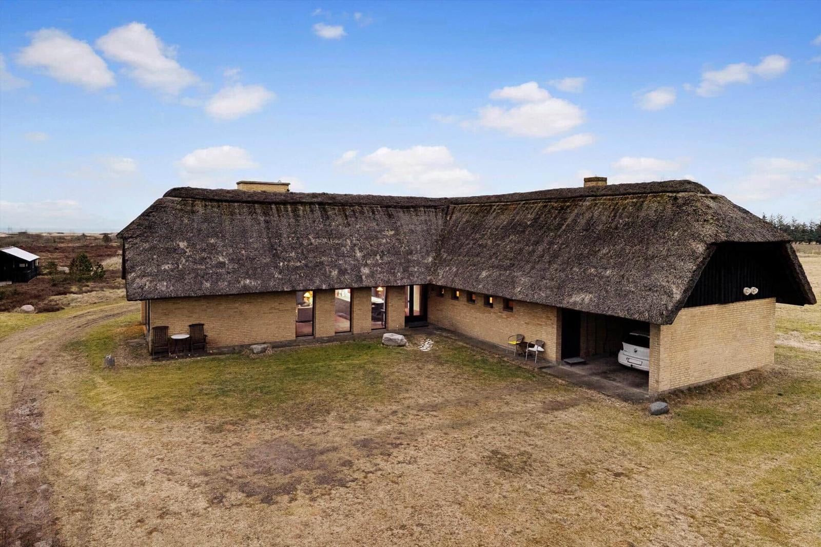 Haus mit Strohdach, Terrasse und Parkplatz im Freien.