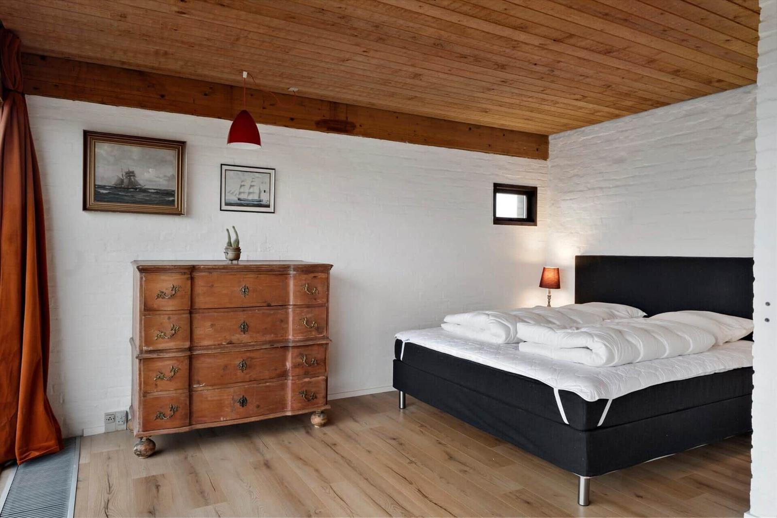 Schlafzimmer mit Holzboden, schwarzer Bettgestell und antikem Schrank.