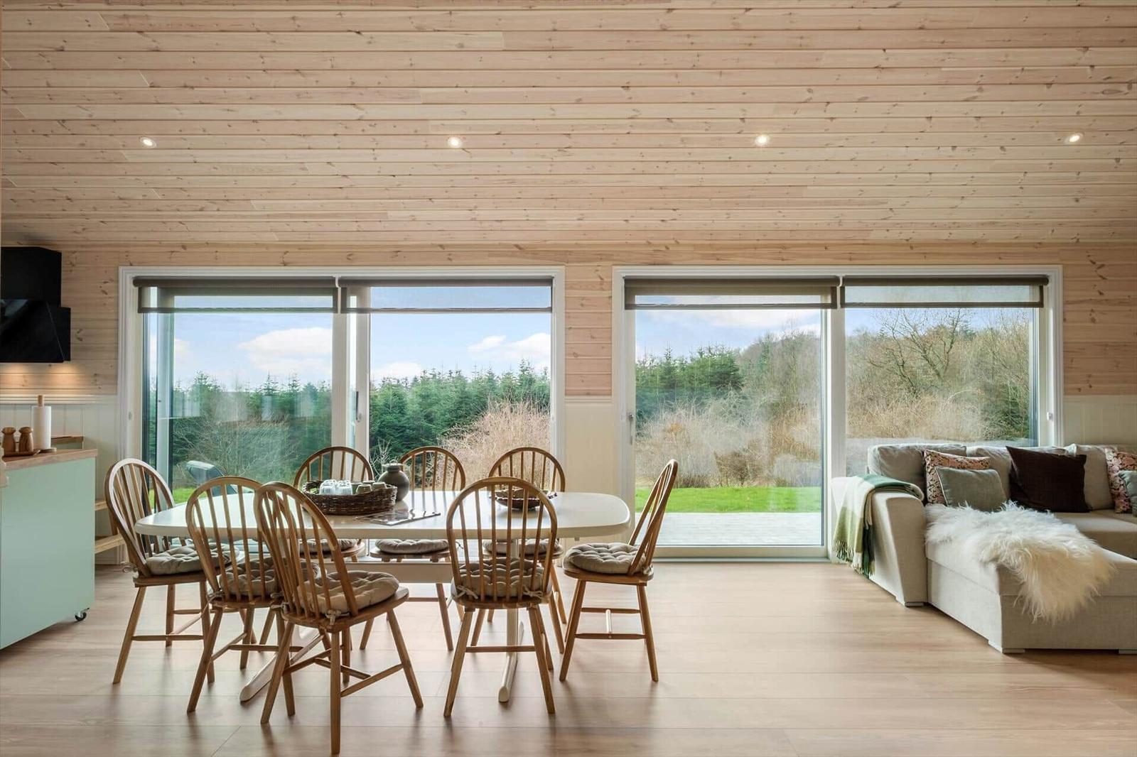 Dining area with table and chairs, sofa and large windows overlooking the garden.