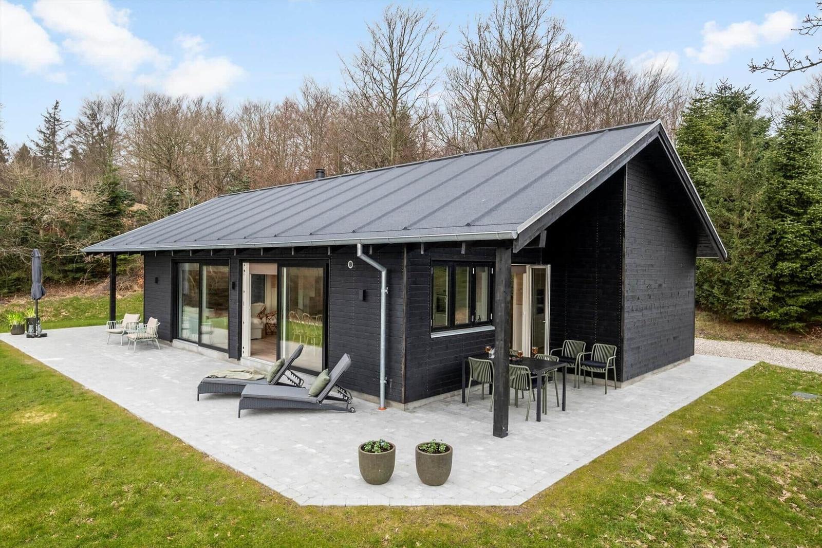 Black house with terrace, loungers, and garden. Modern design with large windows.