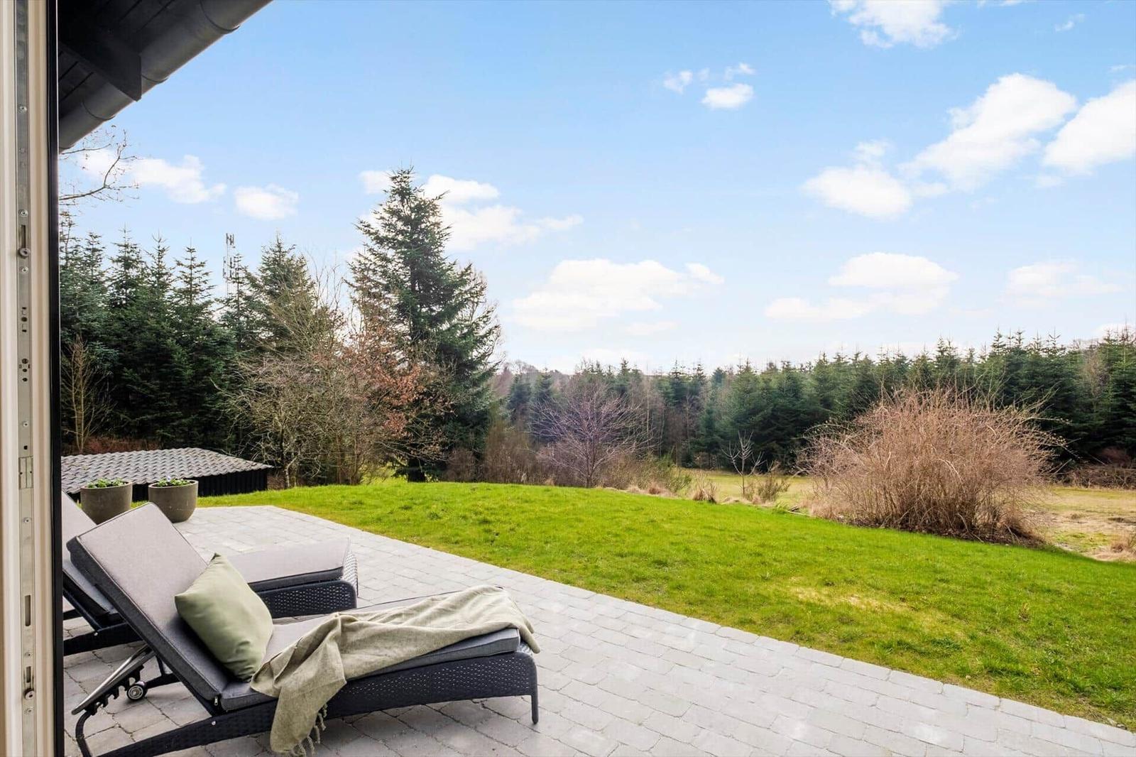Terrace with lounge chairs and view of green lawn and forest.