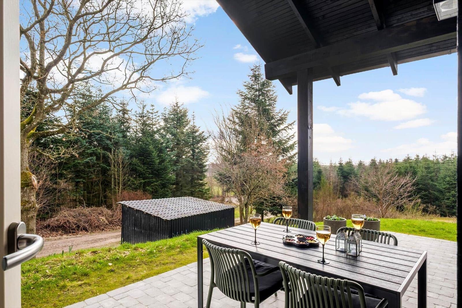 Patio with table and chairs, view of forest and sky.
