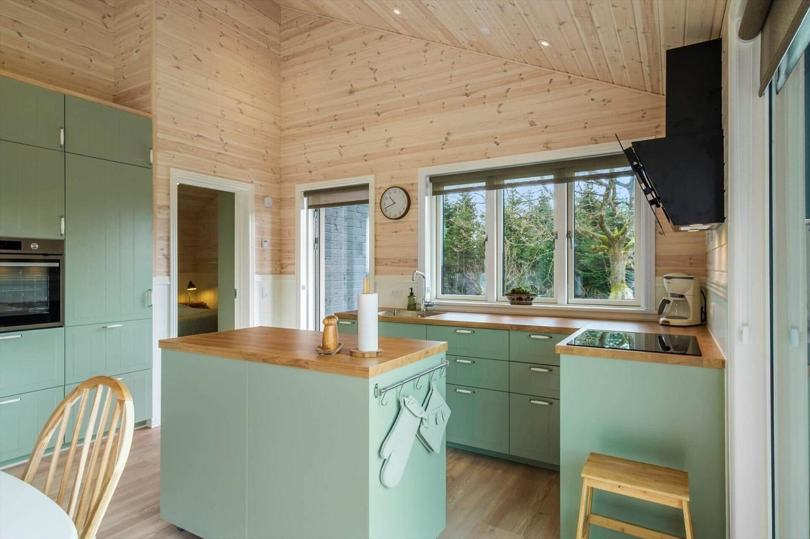 Kitchen with green cabinets, wooden countertop, and view of trees.